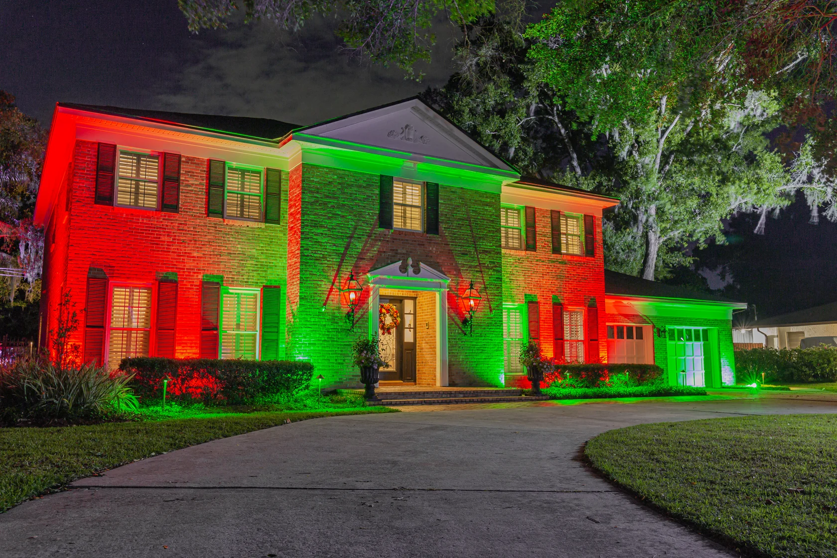 Red and green architectural lighting across a brick home at night.