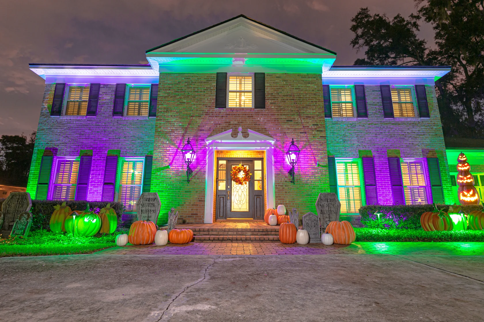 Purple and green lighting across a brick home with Halloween decorations.