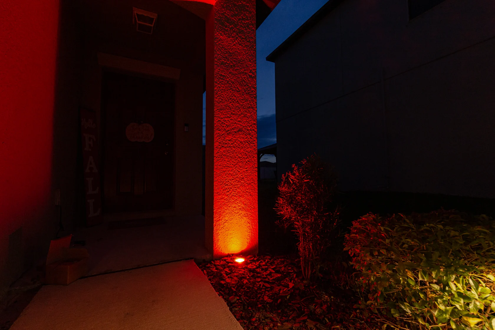 An in-ground light casting red light up a column beside planting beds.